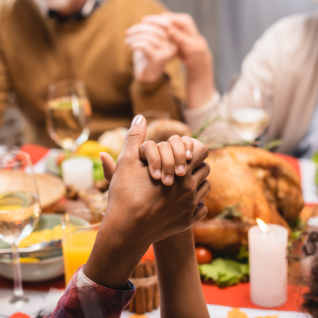 Deux mains entrelacées durant un repas de l’Action de grâce.