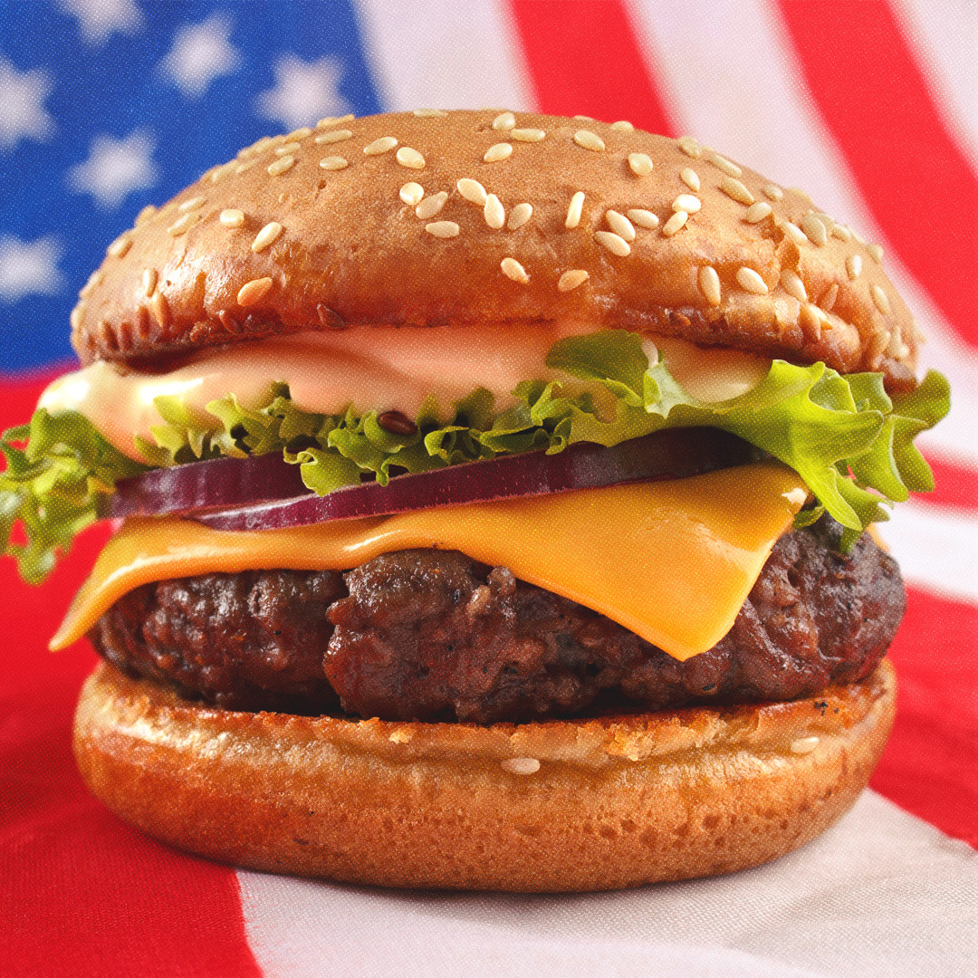 Plan rapproché d’un burger bien garni avec le drapeau des États-Unis en arrière-plan.