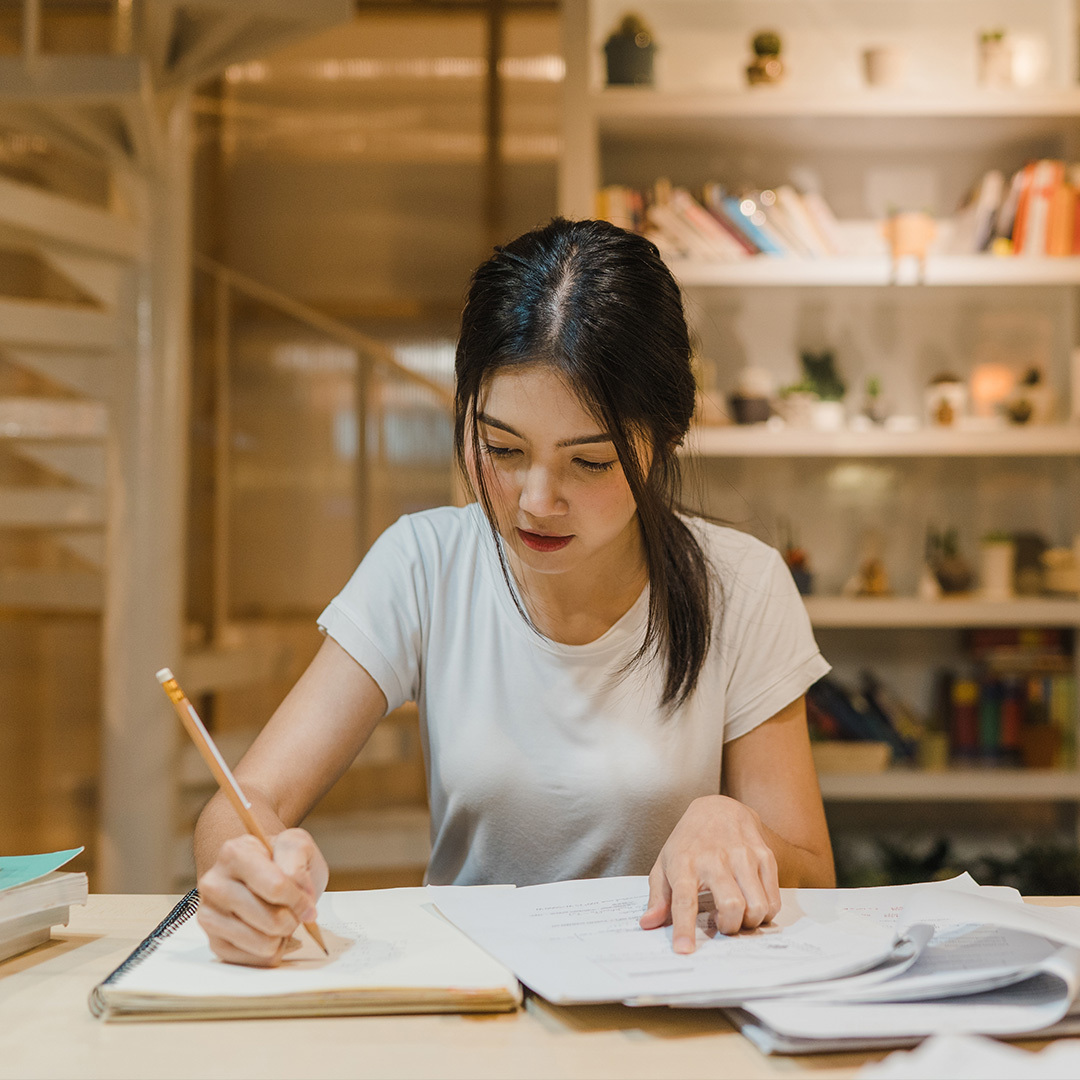 Une jeune fille d’origine asiatique en train d’écrire dans une bibliothèque.