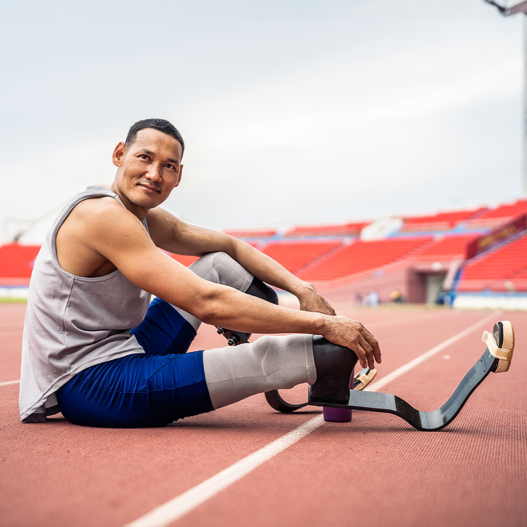 Un athlète asiatique avec des lames prothétiques s’étirant la jambe dans un stade.