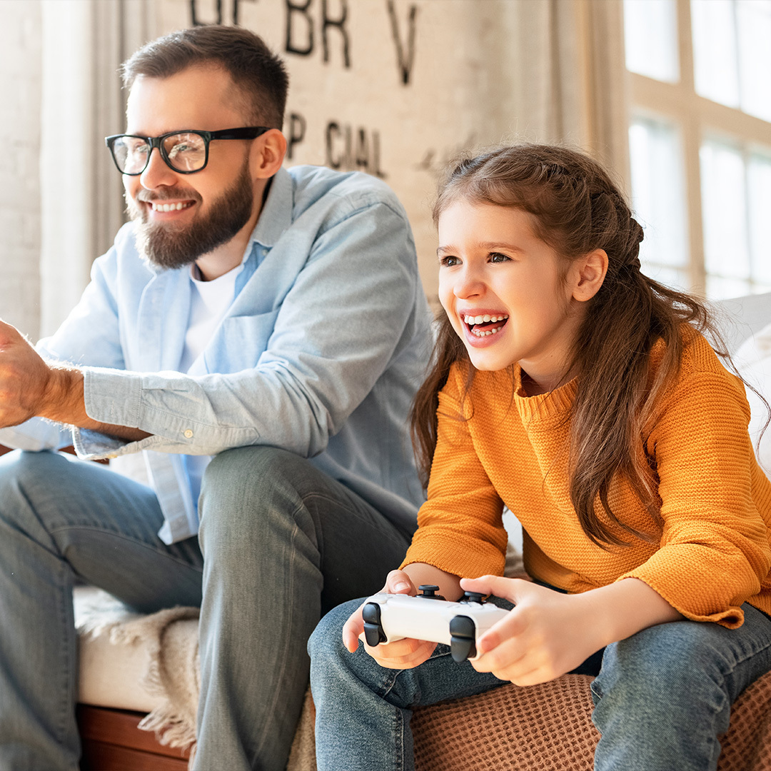 Deux personnes s'amusent en jouant à un jeu vidéo sur console, assis dans un canapé.
