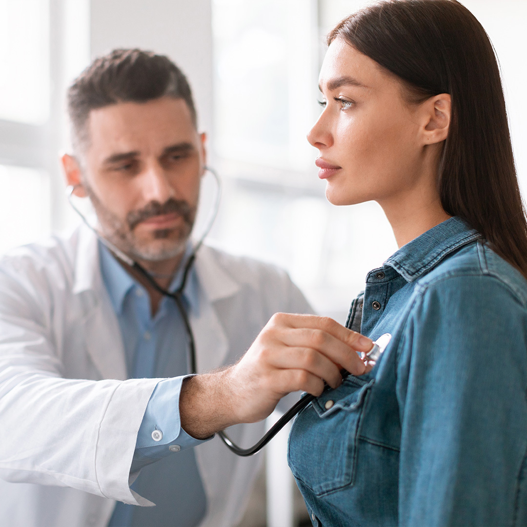 A doctor listens to a woman’s heartbeat through a stethoscope.