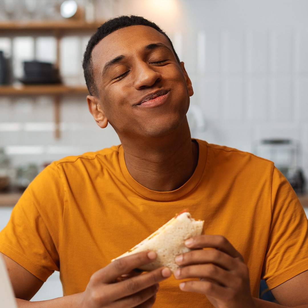 Un homme les yeux fermés tenant un sandwich.