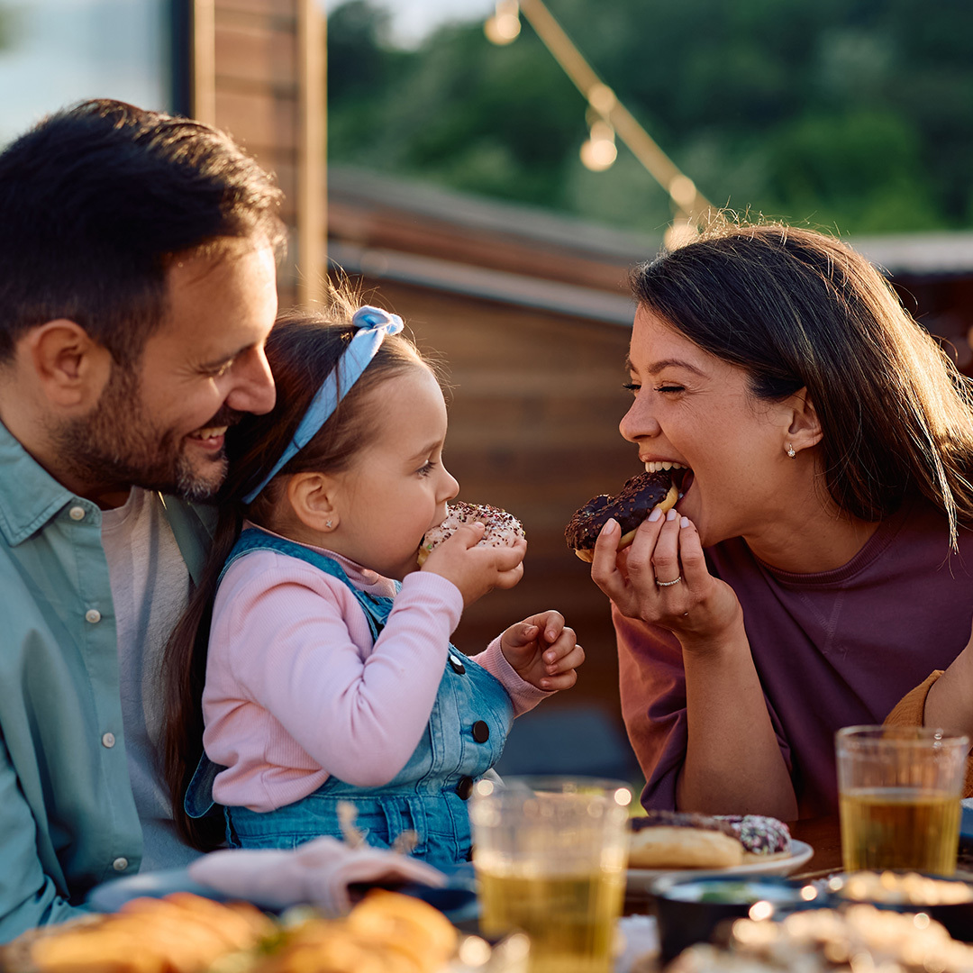 Des enfants heureux et leurs parents mangent des beignets et s’amusent pendant un repas en famille sur une terrasse.