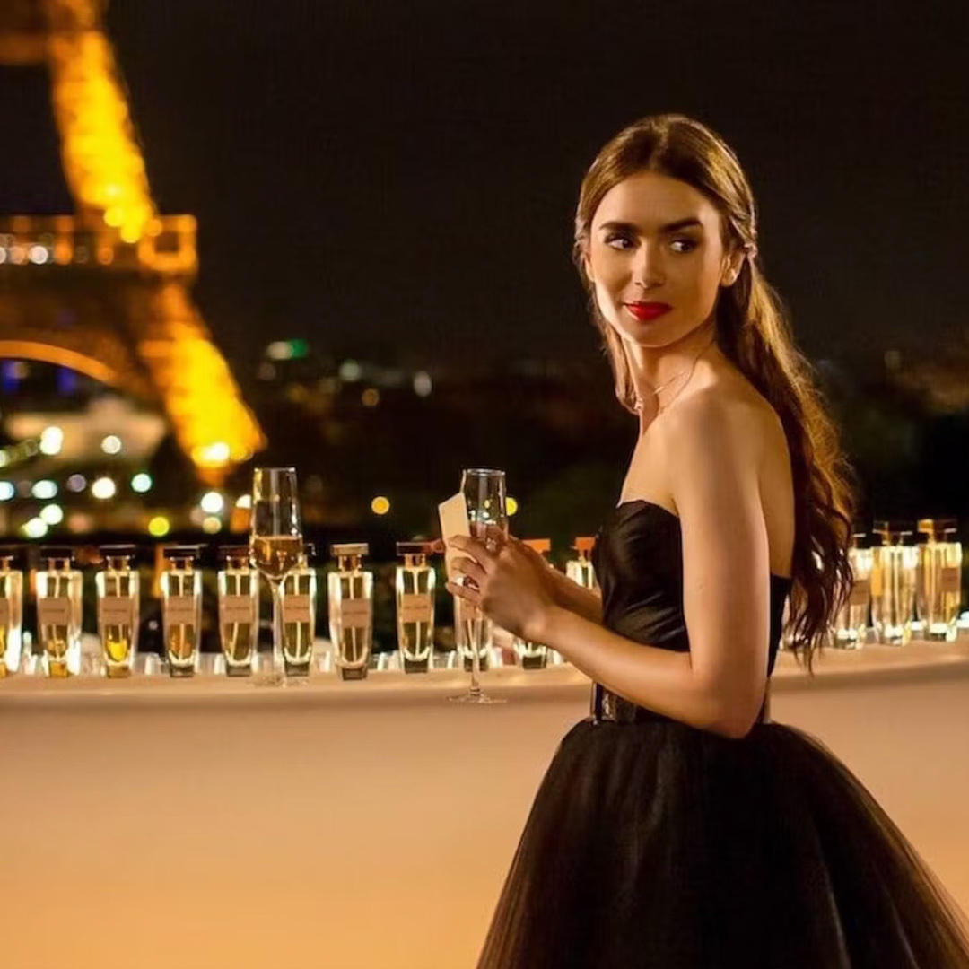 Le personnage d’Emily interprété par Lily Collins dans Emily in Paris, coupe de champagne à la main avec la tour Eiffel en arrière-plan.