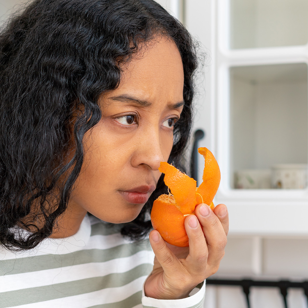 Woman sniffing a peeled orange with a look of concern on her face.