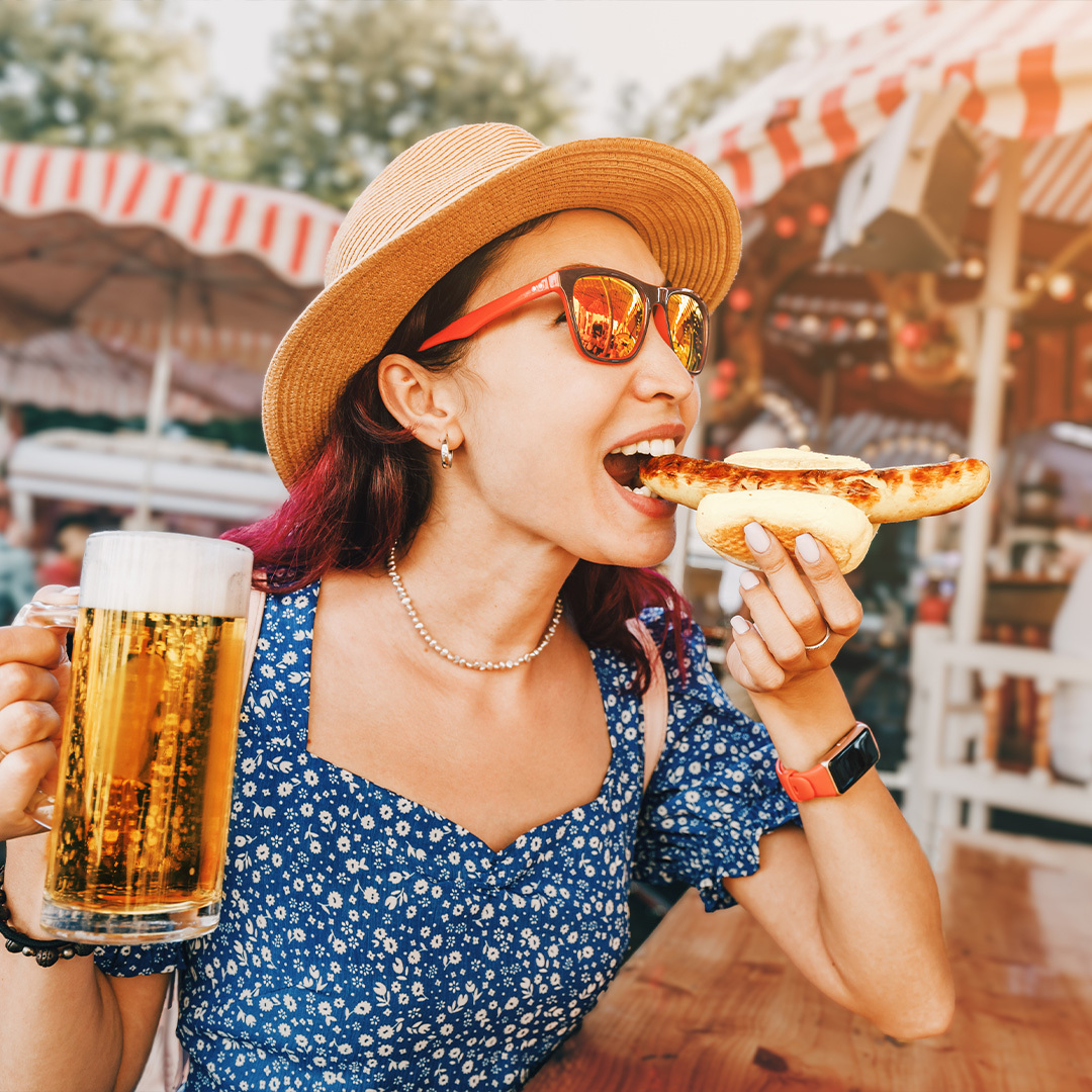 Une jeune femme tenant une bière et mangeant une bratwurst allemande traditionnelle.