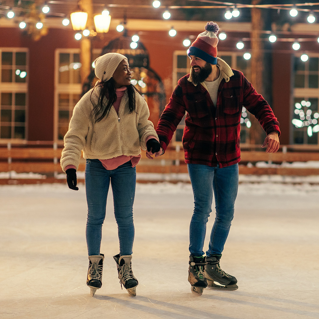 A woman and a man hold hands while ice skating in the park.