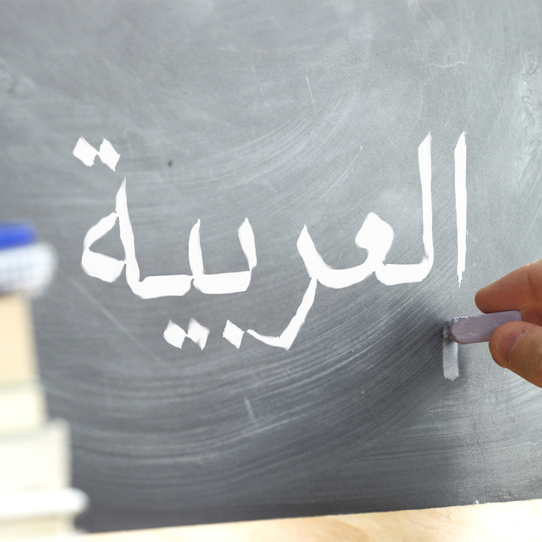 Main écrivant le mot «Arabe» en arabe à la craie sur un tableau.