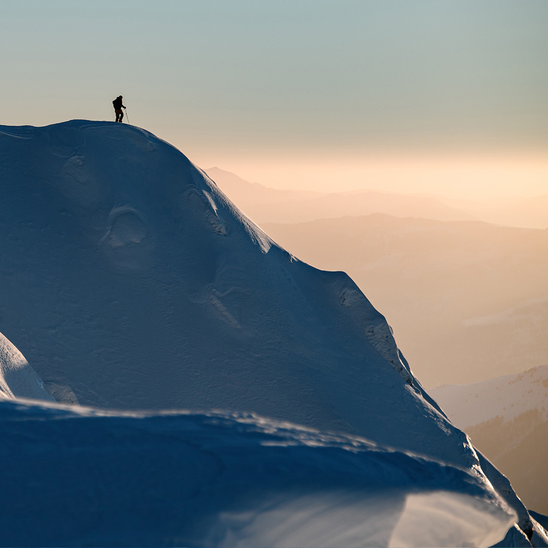 Distant view of a skier standing on a steep, snow-covered mountain.