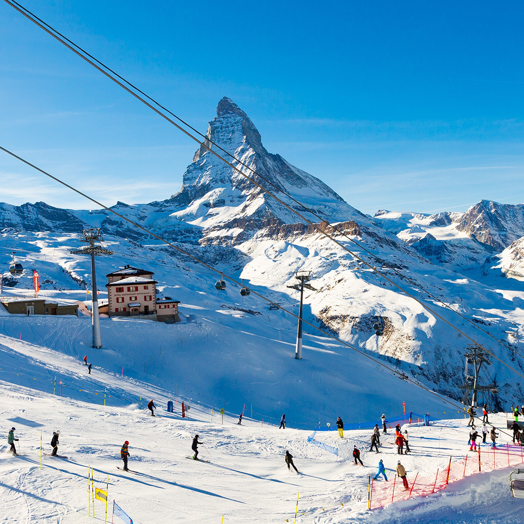 A chairlift and skiers in Zermatt, Switzerland, with a view of the Matterhorn in the distance.