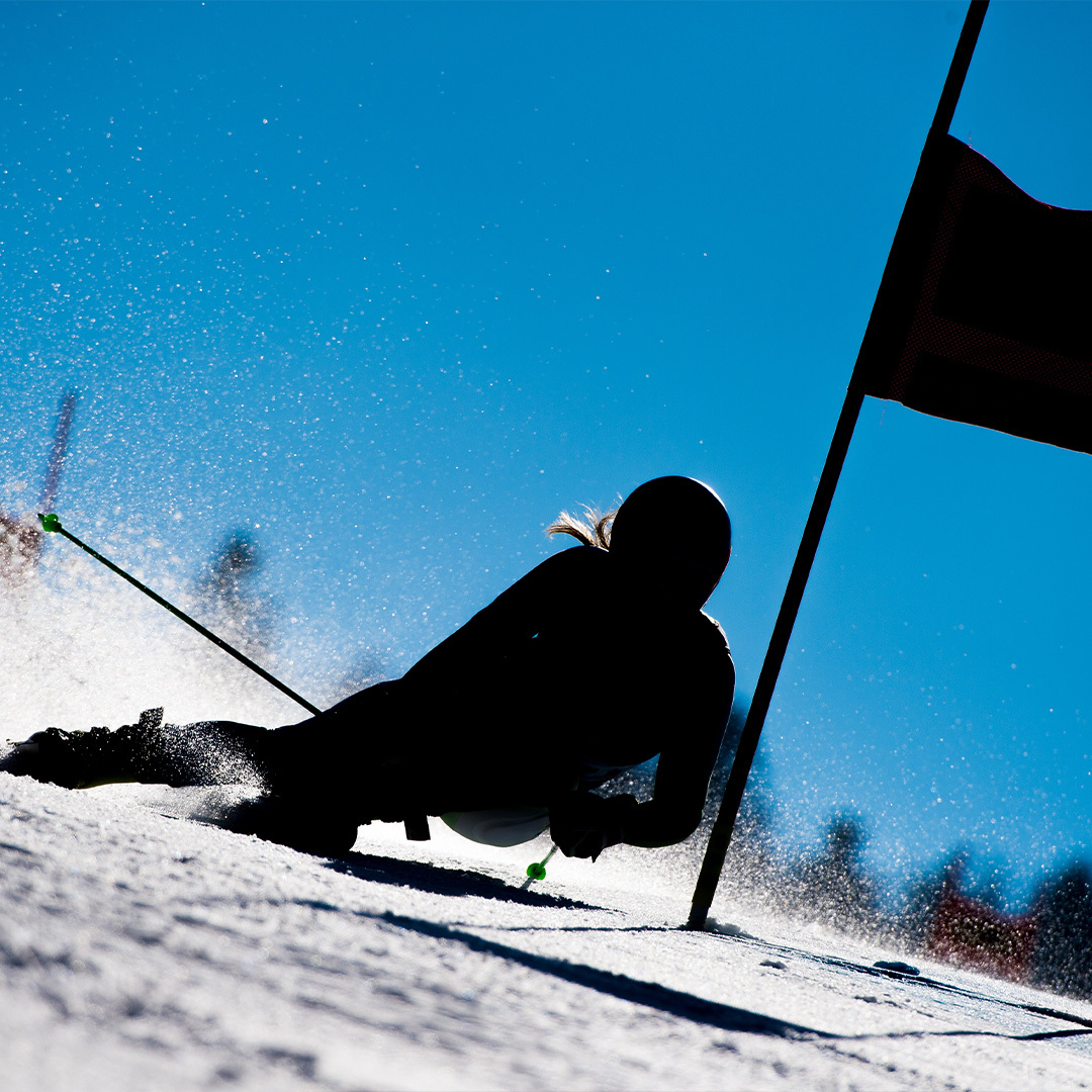 A slalom skier in silhouette descending the slope on a sunny day.