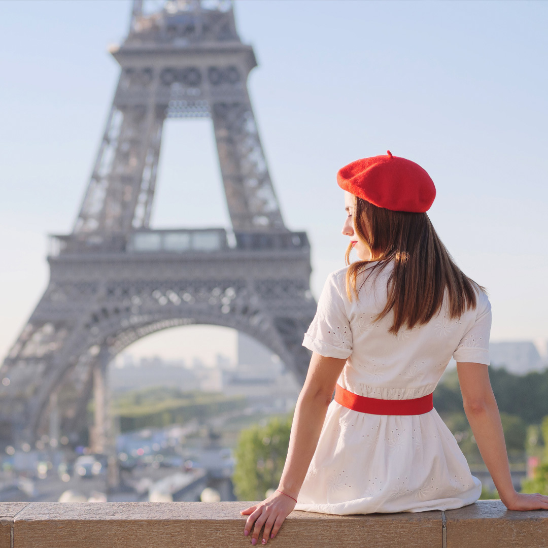 Femme de dos portant un béret, face à la tour Eiffel.
