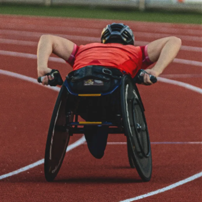 Vue de dos d’un athlète masculin en fauteuil roulant de course sur piste rouge.