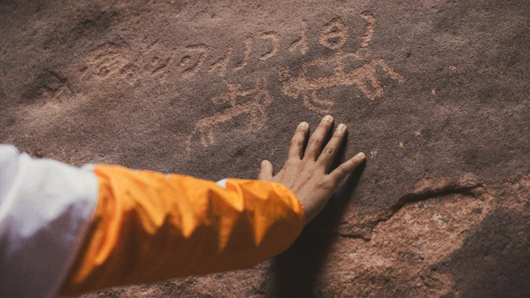 Main posée sur un mur comportant des inscriptions datant d'une ère lointaine.