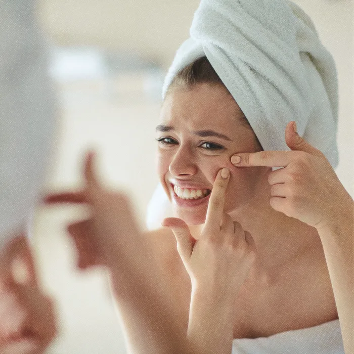 Femme se regardant dans le mirroir pour se percer un bouton.